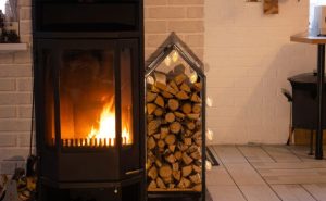 Poêle à bois moderne noir avec une vitre laissant voir des flammes, à côté d'un casier décoratif rempli de bûches et de lumières.