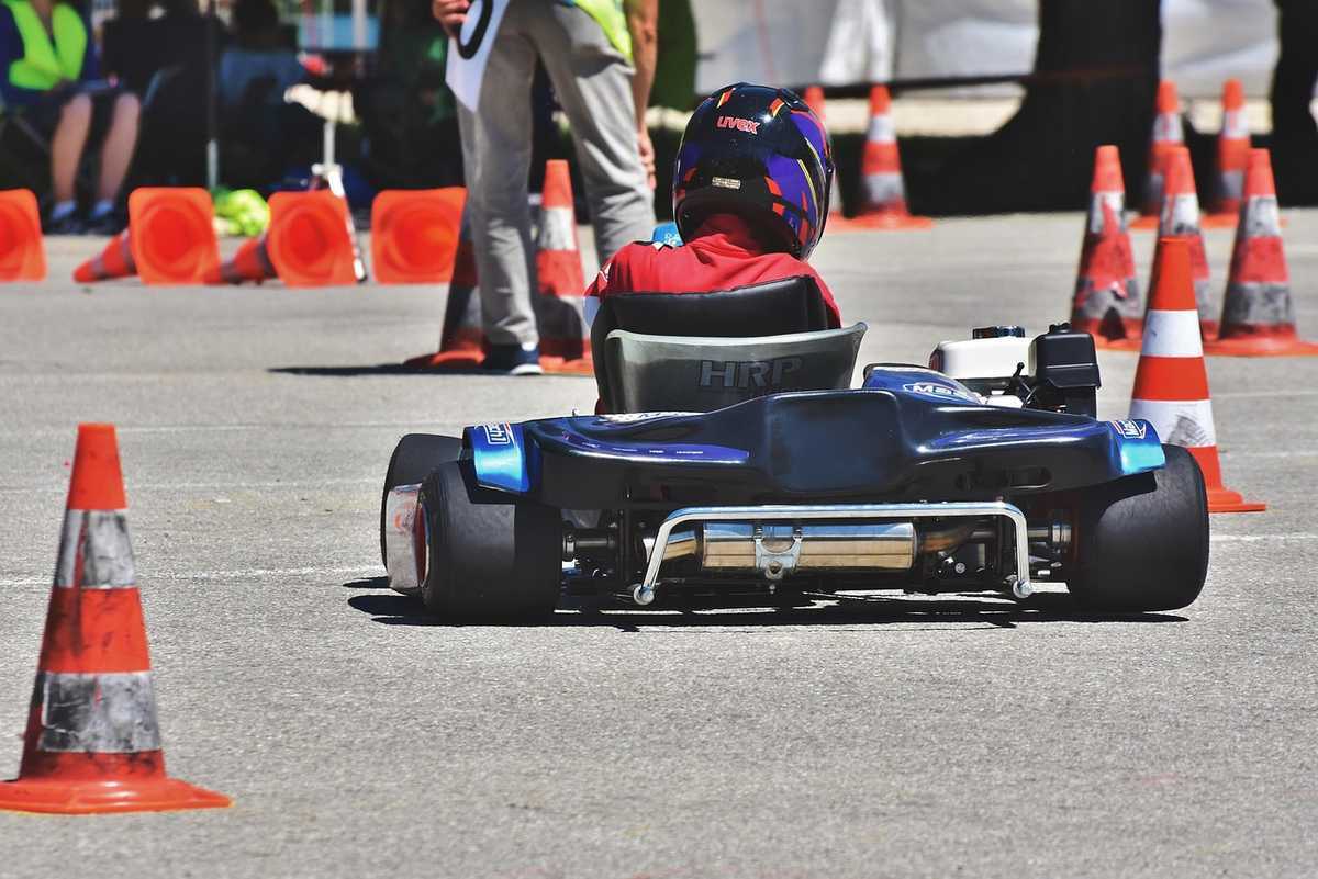 Enfant pilotant un kart noir sur circuit avec cônes orange de délimitation et spectateurs en arrière-plan Enfant pilotant un kart noir sur circuit avec cônes orange de délimitation et spectateurs en arrière-plan