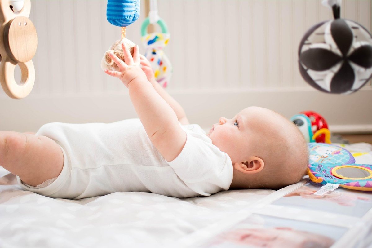 Bébé nu allongé, jouant avec des jouets suspendus, ballon noir et blanc visible