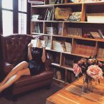 Une femme lit un livre dans un fauteuil en cuir, bibliothèque