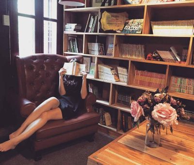 Une femme lit un livre dans un fauteuil en cuir, bibliothèque