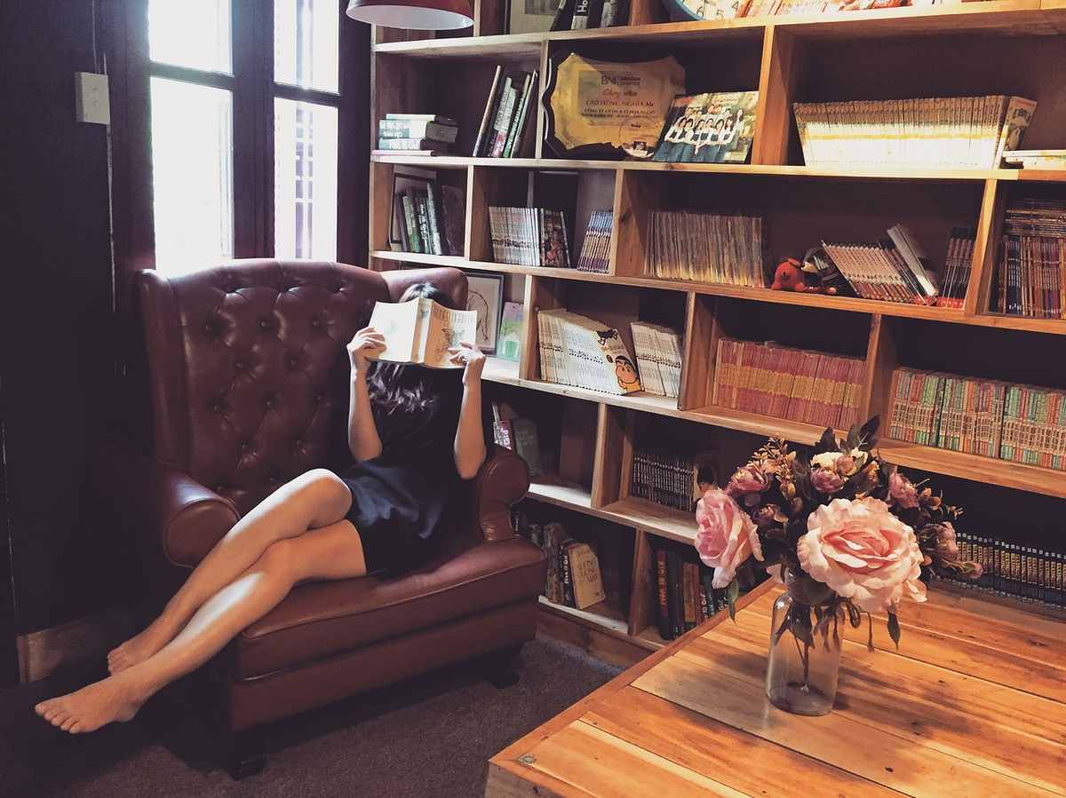 Une femme lit un livre dans un fauteuil en cuir, bibliothèque