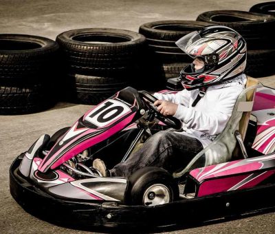Un conducteur pilote un kart rose sur circuit avec pneus empilés