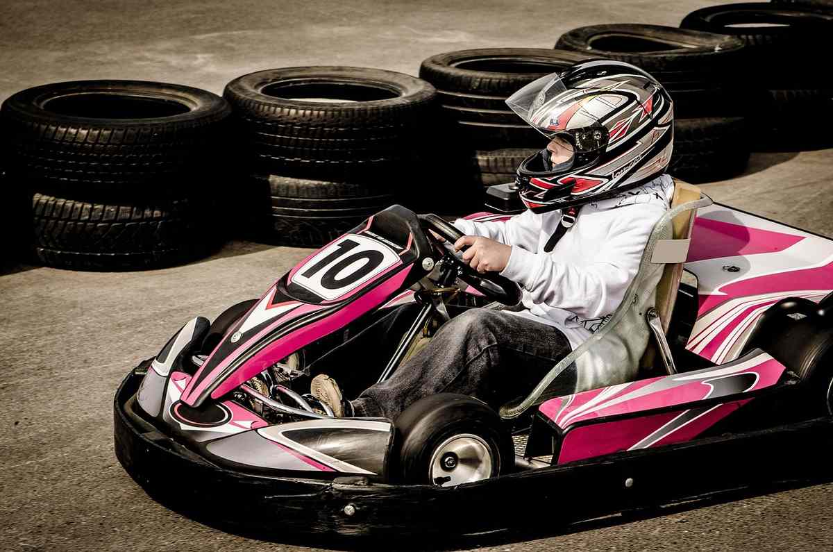 Un conducteur pilote un kart rose sur circuit avec pneus empilés
