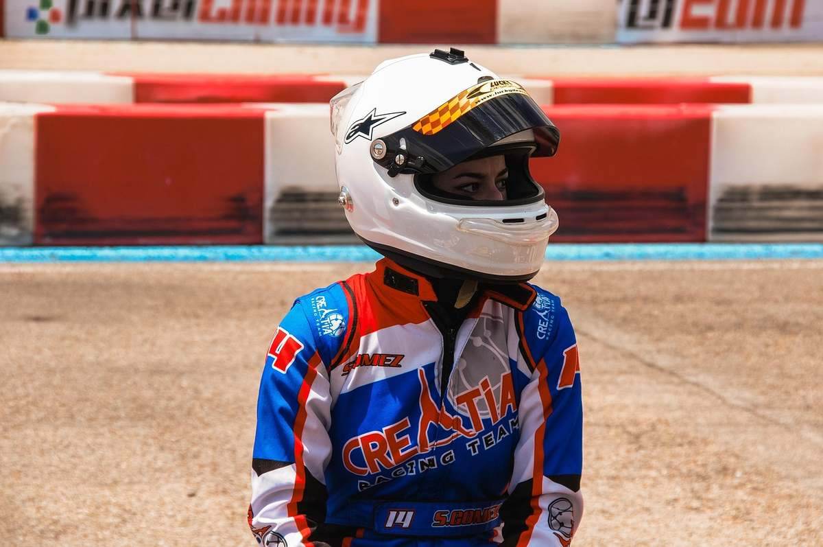 Pilote de course en combinaison bleue et rouge, portant un casque blanc, sur une piste de course