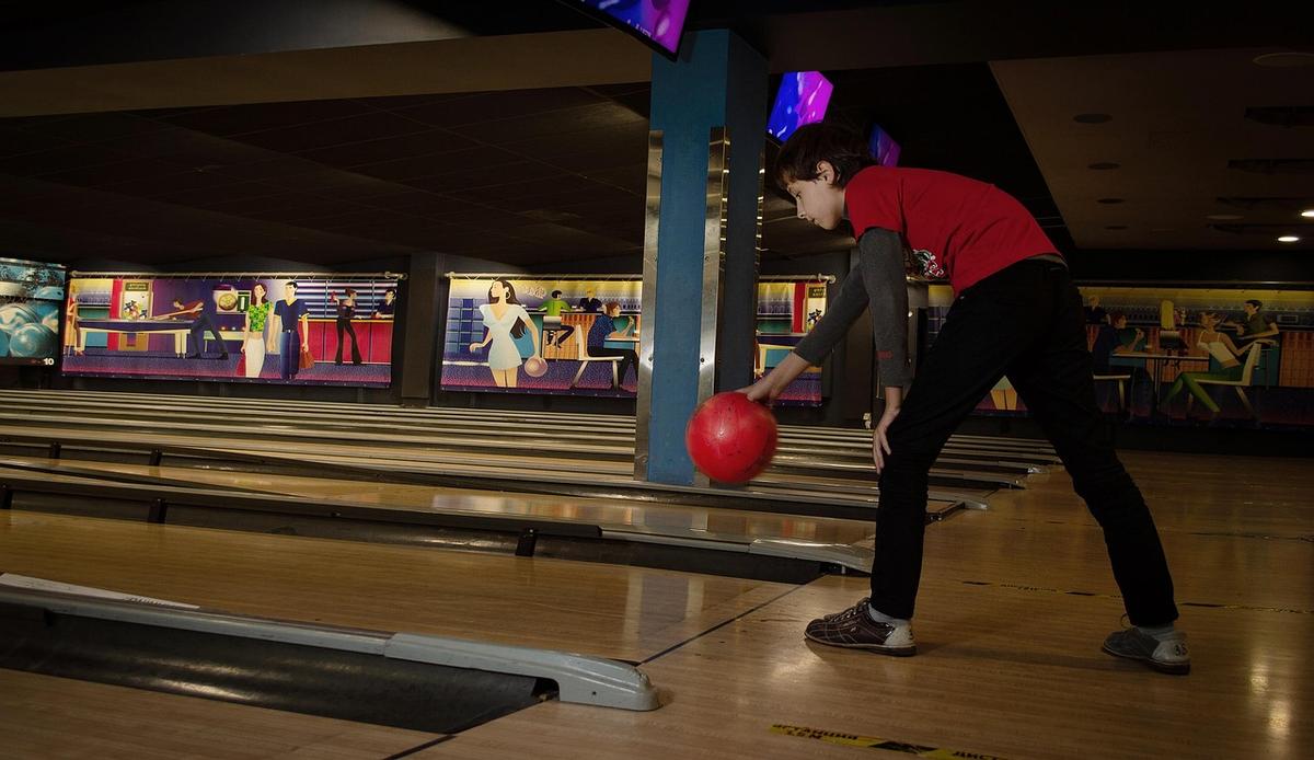 Un joueur lance une boule rouge sur une voie de bowling
