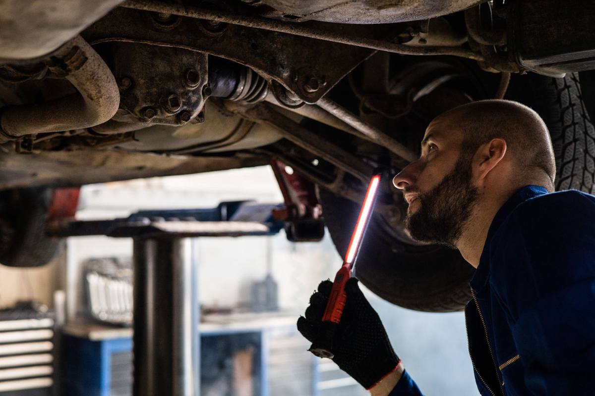 Mécanicien examine sous un véhicule avec une lampe torche dans un atelier