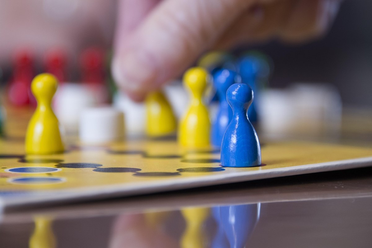 Une main déplace un pion bleu sur un plateau jaune