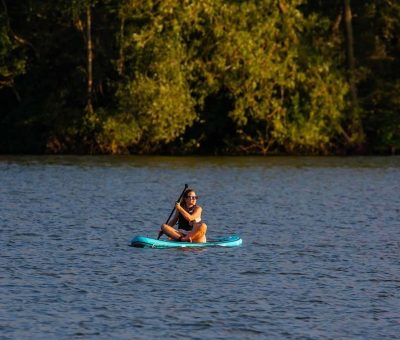 Une personne pratique le stand up paddle sur un lac calme entouré de forêt