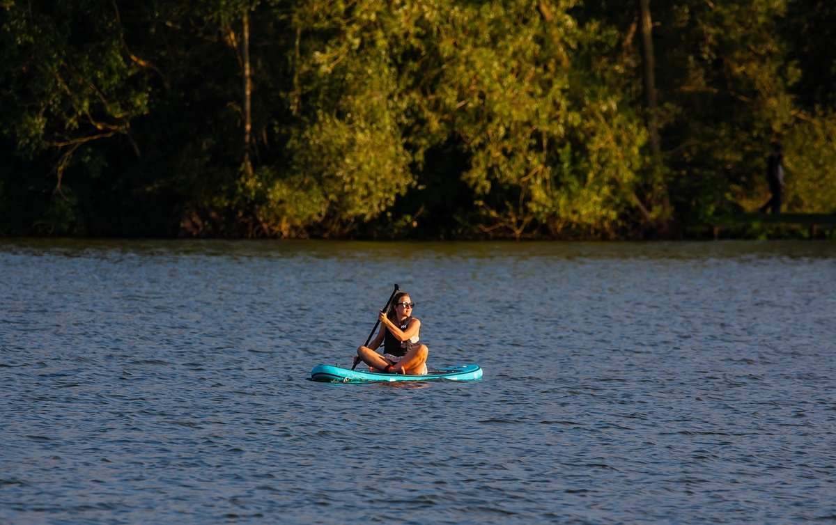 Une personne pratique le stand up paddle sur un lac calme entouré de forêt