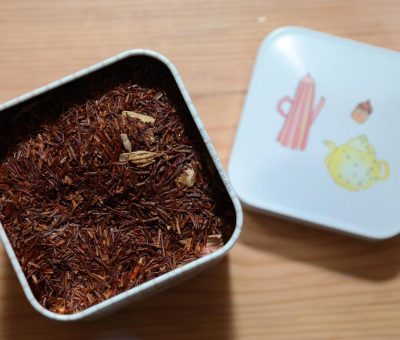 Boîte métallique contenant du rooibos, couvercle décoré, posé sur bois