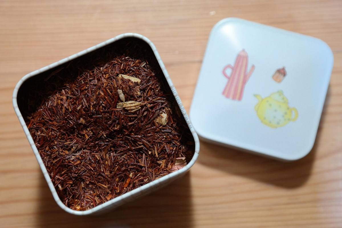 Boîte métallique contenant du rooibos, couvercle décoré, posé sur bois