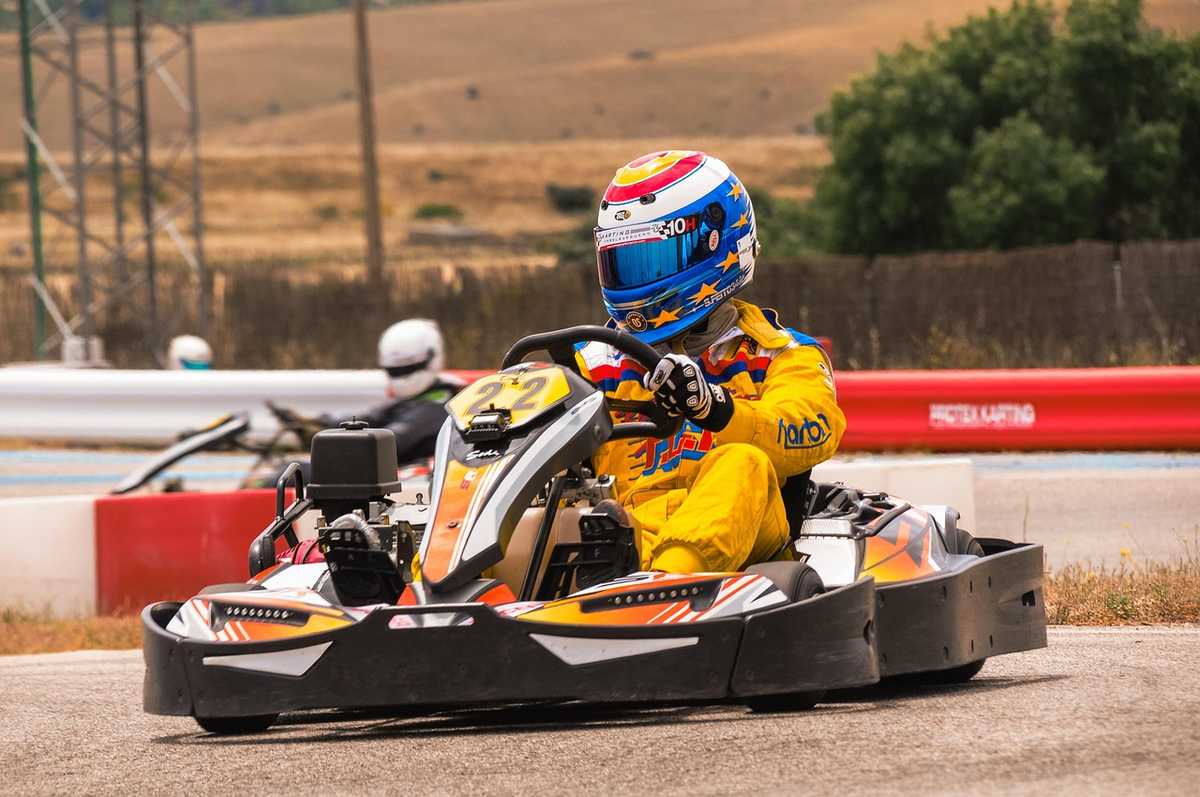 Pilote en kart jaune et casque coloré conduisant sur piste Pilote en kart jaune et casque coloré conduisant sur piste