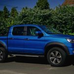 Voiture utilitaire bleue stationnée sur route feuillage verdoyant derrière