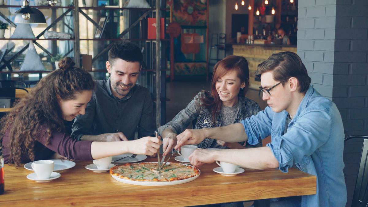 Quatre amis partagent une pizza autour d'une table en bois