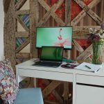 Un bureau blanc avec ordinateur, écran, chaise et vase de fleurs
