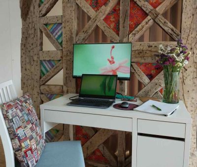 Un bureau blanc avec ordinateur, écran, chaise et vase de fleurs