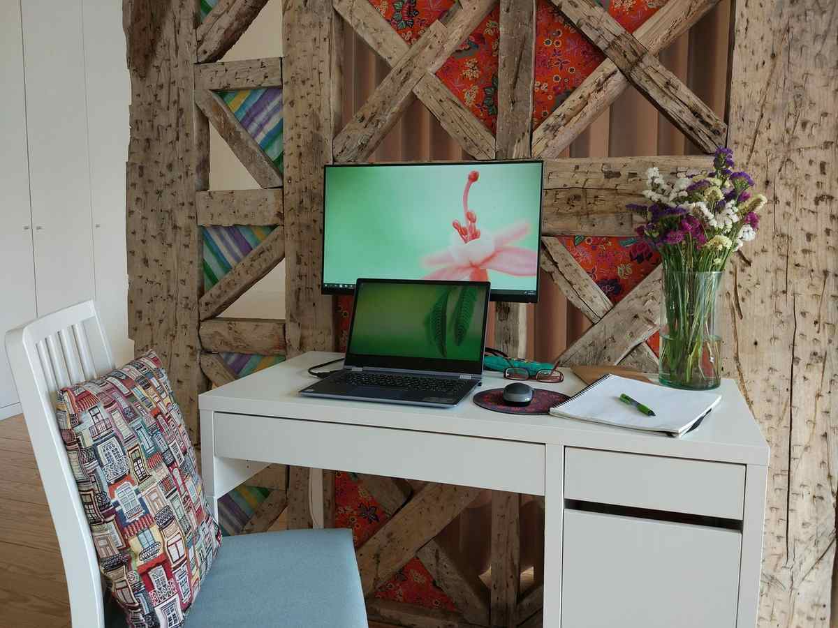 Un bureau blanc avec ordinateur, écran, chaise et vase de fleurs